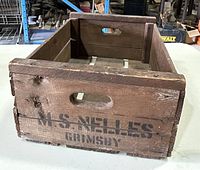 Front angled view of the wooden box showing M. S. Nelles Grimsby branding and cut-out handle, emphasizing wood texture and wear.