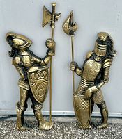 Two vintage brass knights in armor standing side by side, holding halberds and shields with embossed decorative designs.