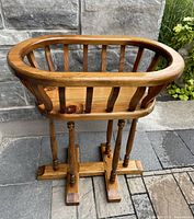 Side view of vintage solid pine wood plant stand showing oval slatted top and turned leg base on stone tile surface.