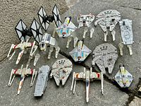 Top-down photo showing various Star Wars model spaceships placed on stone ground surface, with multiple Millennium Falcons and X-Wings visible.
