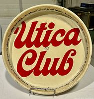 Front view of the circular cream-colored metal advertising tray with large red 'Utica Club' lettering and border text slogan.