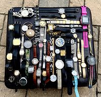 Top-down photo showing 31 assorted watches and pocket watches arranged on a black mat, featuring a mix of strap materials and watch types.