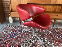 Angled view of red leather swivel armchair showing curved seat, backrest and polished steel five-star base