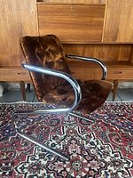 Angled side view showing cantilever tubular chrome frame, curved armrest and tufted seat and back upholstery