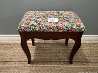 Front view of vintage wooden bench stool with floral upholstered seat showing curved legs and wood finish.