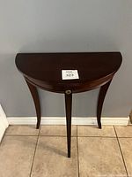 Front view of the vintage halfmoon side table showing the dark brown wood finish, curved legs, and brass floral knob detail.
