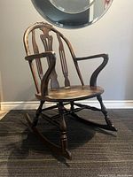 Side view of the vintage Windsor style rocking chair showing curved backrest and armrest, turned legs on rockers.