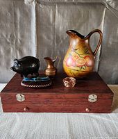 Full lot on box: ceramic pitcher, bronze pitcher, black piggy bank, copper napkin ring on wood storage box