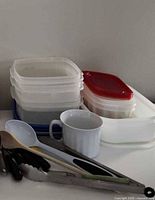 stacked plastic food containers, ceramic mug, assorted utensils visible