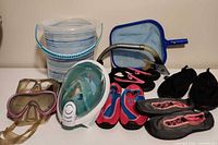 Group shot of all items laid out: bucket, skimmer net, snorkel mask, snorkel, two goggles, four pairs water shoes