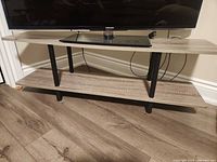 Front view of two-tier grey wood grain TV stand with black legs