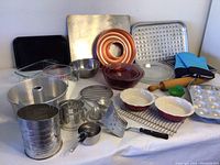 Front angled photo of the full assortment showing nesting Pyrex bowls, muffin tins, pie pans, measuring cups, cooling racks, spatula, sifter, and oven mitts