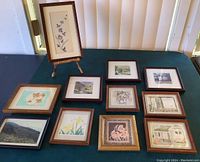 Overall view of lot showing 10 framed prints laid on green surface, and one print displayed upright on bamboo stand.
