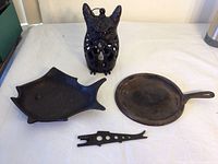 Photo showing four cast iron pieces: an owl candle holder, fish pan, small round griddle, and small fish-shaped piece.