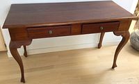 Front view of the console table showing two drawers and curved legs on a light wooden floor.