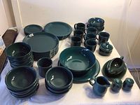 Large assortment of green glazed Dansk and unmarked plates, bowls, mugs along with green serving pieces and Gibson pitcher, arranged on table.