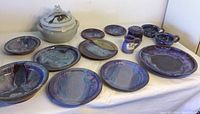 Wide view of the full pottery set showing dinner plates, small plates, mugs, bowls, large platter, and lidded ceramic piece with frog decorations.