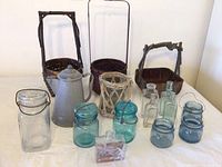 Full view of all items showing 2 Blue Ball blue glass jars, clear vintage bottles, grey speckled coffee pot, 3 rustic woven baskets, and rattan wrapped candle holder.