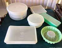 Photo showing top view of assortment of vintage Tupperware containers in various shapes, translucent white and colored plastic, with lids on some.