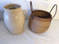Milk urn and woven basket side by side on white surface