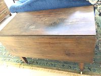 Side view of vintage solid wood drop leaf table showing wood surface wear and casters on legs