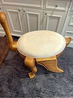 Full side view of the birdlike wooden stool with fabric seat and gold accents, showing shape and structure.