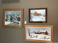 Three paintings hung on wall: snowy street scene (top left), barn scene by G.W. Burton (top right), barn and fence scene by Thys Presing (bottom)
