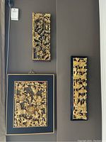 Three panels arranged on wall—two framed on black backboards, one unframed relief at left.