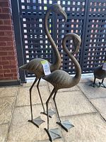 Pair of metal flamingo statues standing on patio in front of lattice screen