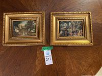 Two framed fabric paintings side by side on a table highlighting their size and frames.