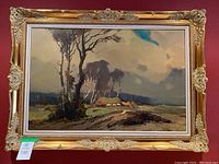 Full frontal view of oil painting in ornate gilt frame hung on red wall showing rural landscape with trees and cottages