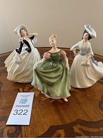 Photo showing three Royal Doulton figurines Autumn Breezes, Michele, and Margaret placed on a wooden inlaid table, front view.