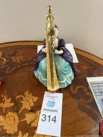 Front view of the figurine showing seated woman in purple and turquoise gown playing gold-tone harp