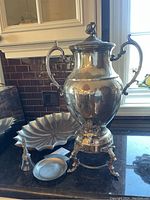 Photo showing full view of the silver coffee percolator on warming stand, large tray to the left, small dish and decorative bell to the front.