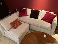 Full view of off-white sofa bed and matching armless chair with four decorative pillows against red wall.