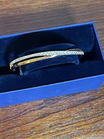 Rose gold colored Swarovski bracelet with clear crystals placed in blue box on wood surface.