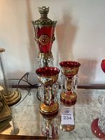 Front view of red table lamp and two red glass mantle glasses on mirrored surface