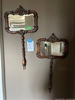 Two carved wood handle wall mirrors side by side mounted on wall