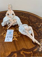 Overview of both porcelain ballerina figurines on a wooden table showing size and details.