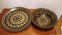 Wide view showing the large plate and bowl set together on a wooden surface highlighting the olive green tone and geometric circle pattern.