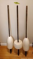 Set of three vintage antique buoys with wooden rods, displayed standing against a wall on a hardwood floor