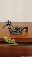 Front side view of bronze seahorse incense dish showing head, body, and tail details on a wooden surface.