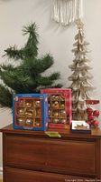 Photo showing two artificial Christmas trees (green and gold), two boxes of ornaments, and small decoration items.