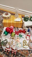Photo of assortment of vintage Christmas decorations including balls, candle holders, light-up angel, and various figures on a carpeted floor.