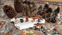 Photo showing six vintage wooden hand-made Christmas ornaments positioned in front of an array of pine cones of various sizes and types on a patterned rug.