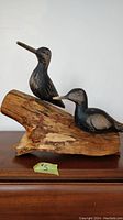 Front view of two black painted wooden birds carved and mounted on knotty driftwood.
