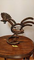 Full profile view of the hand-fabricated metal rooster sculpture on a wooden table, showing overall form and aged metal parts.