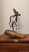 Front view of metal and wood sculpture showing dragonfly atop bullrushes mounted on wooden base.