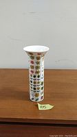Front view of slender white vase with colorful floral grid design on wood surface.