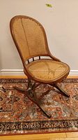 Full view of the antique rocking/bouncer chair showing cane seat and backrest with wooden frame and metal base.